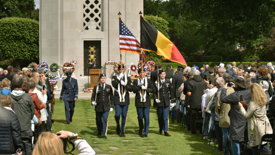 Militairen marcheren voor het monument met Amerikaanse en Belgische vlag