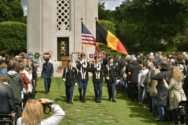 Militairen marcheren voor het monument met Amerikaanse en Belgische vlag